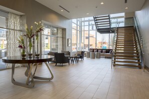A spacious hotel lobby with a modern staircase, a dining area with a round table, and large windows offering views of the city. - DoubleTree by Hilton Evansville (Evansville)