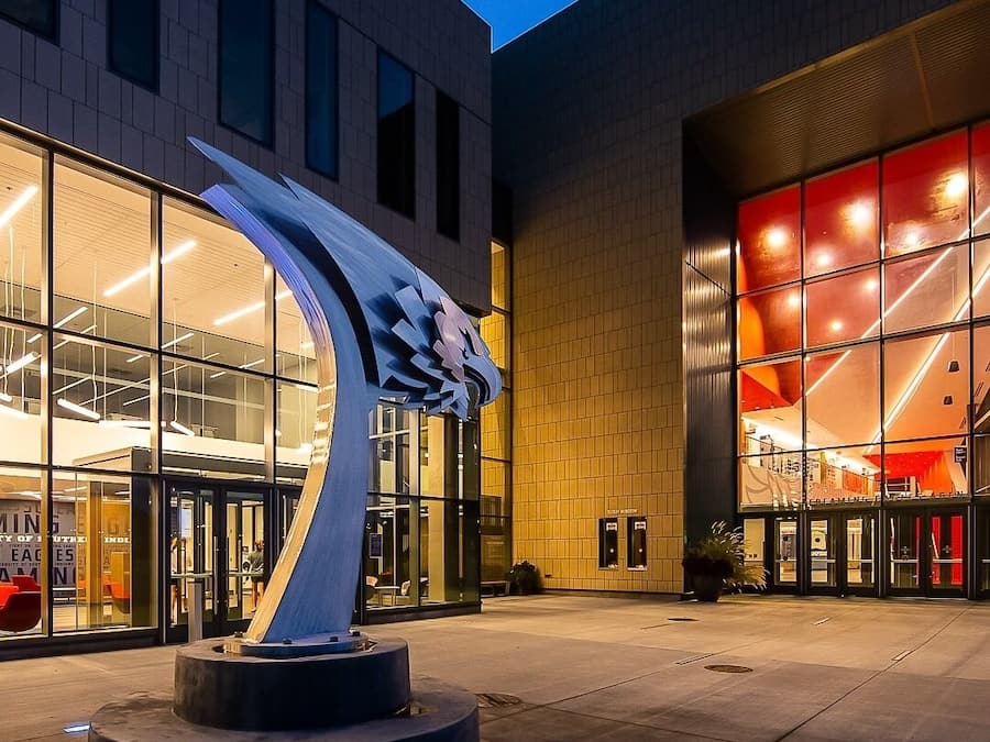 A modern building with a prominent sculpture in front, large glass windows, and a brightly lit entrance.