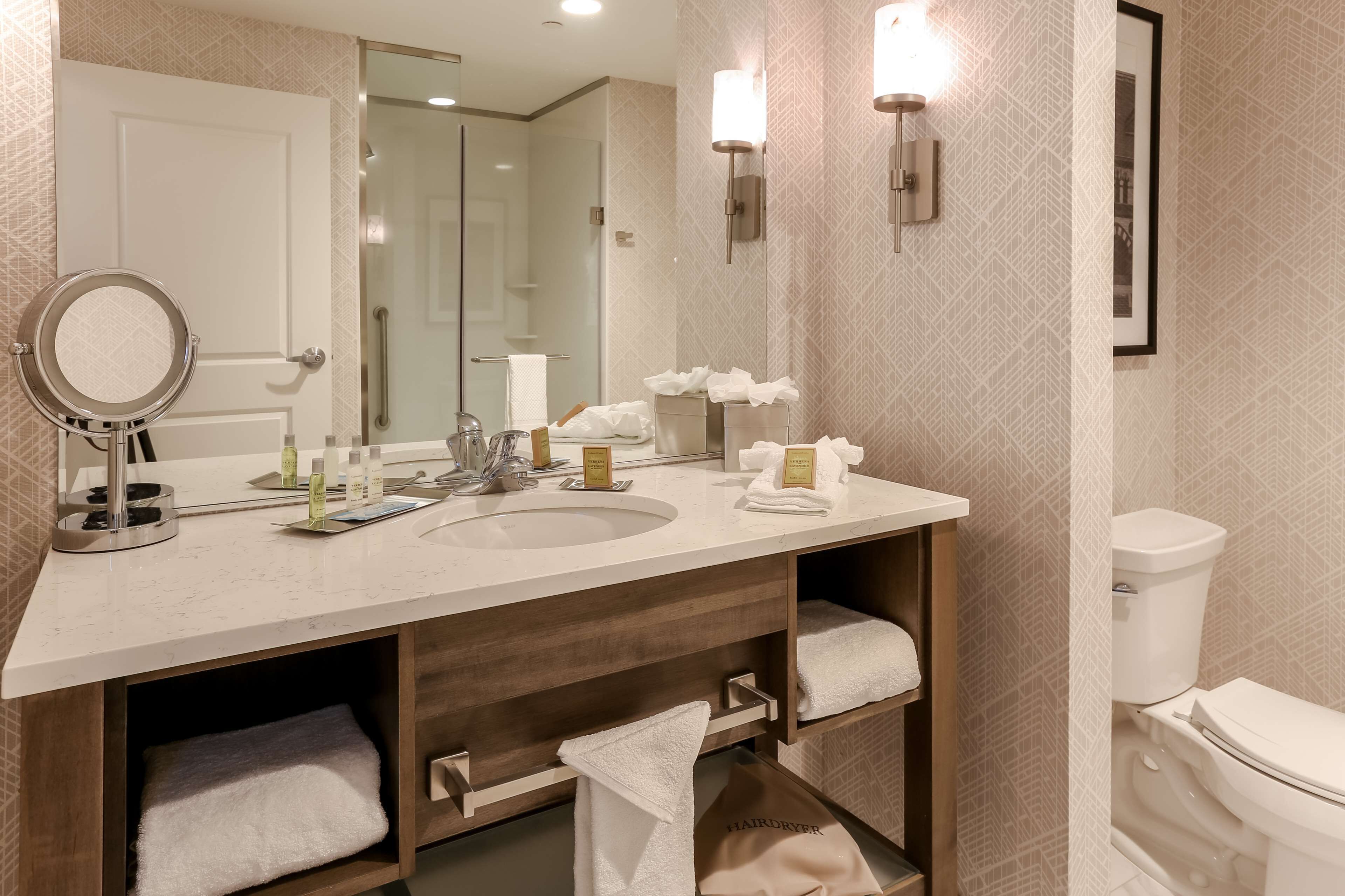 Un bagno moderno con un ampio specchio, due lavabi e un water. Asciugamani e articoli da toilette sono presenti sul mobile.