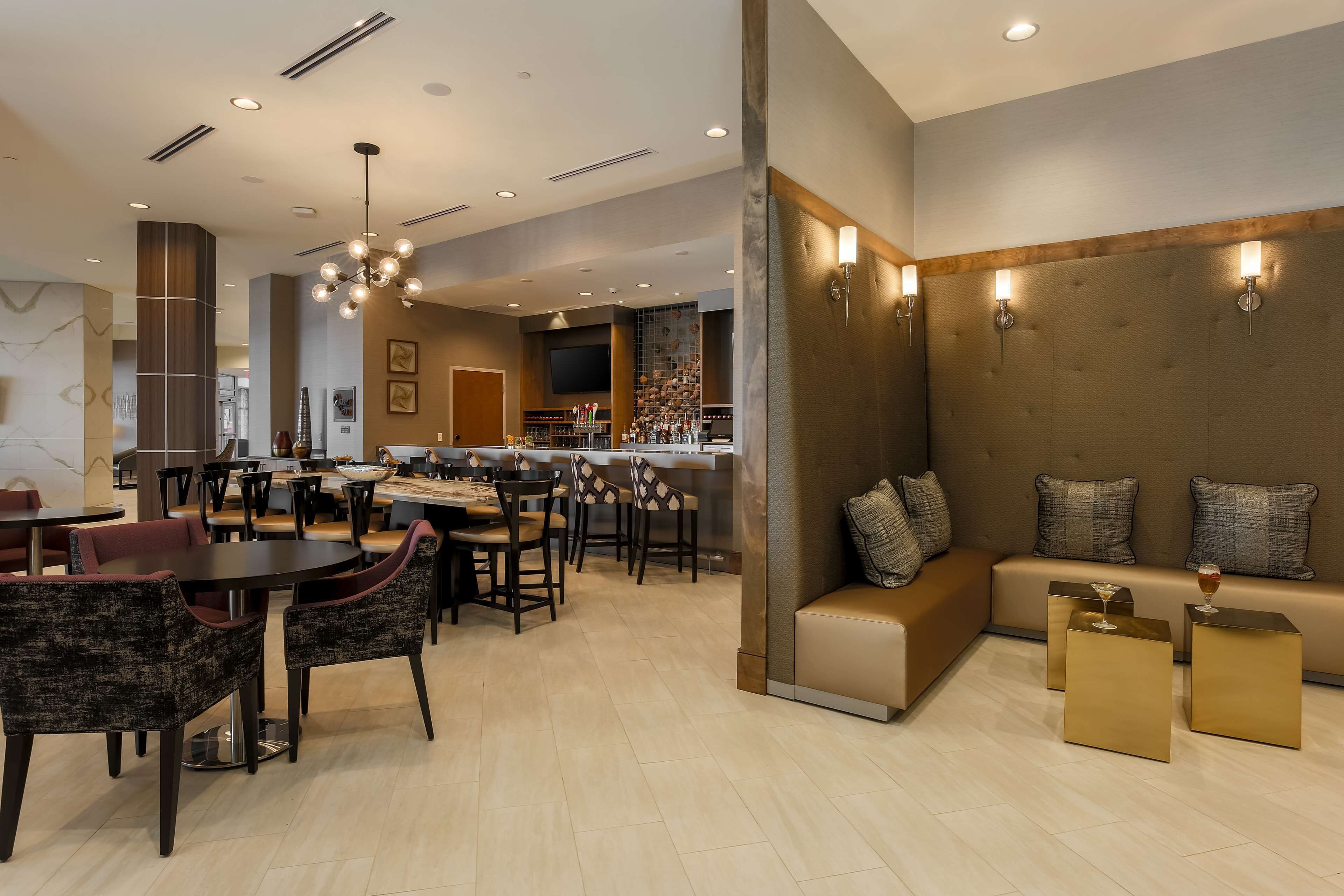 A modern hotel lobby with a bar area, seating arrangements, and a television screen.