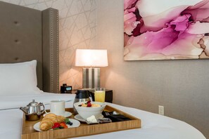 A neatly made breakfast tray on a bed with a coffee pot, croissant, and fruit bowl. - DoubleTree by Hilton Evansville (Evansville)