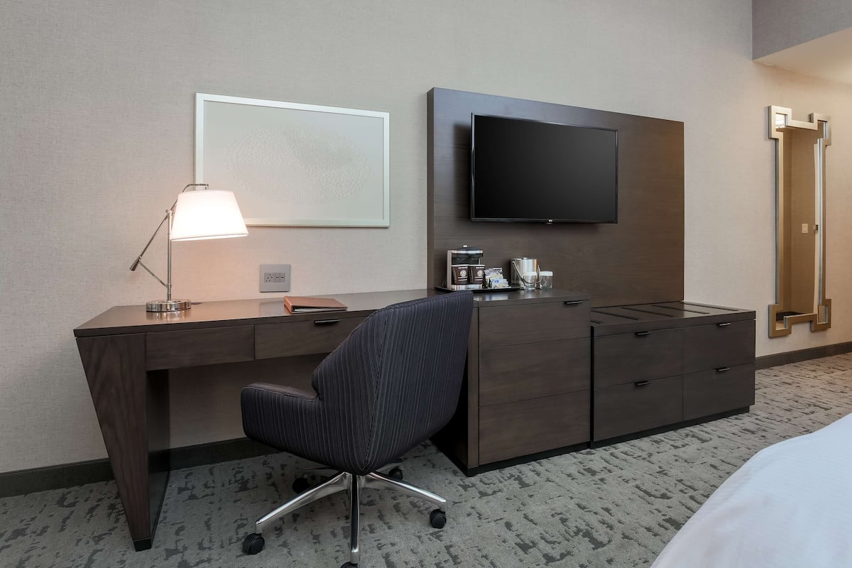 A hotel room with a wooden desk, a chair, a flat-screen TV, a coffee maker, and a bed.