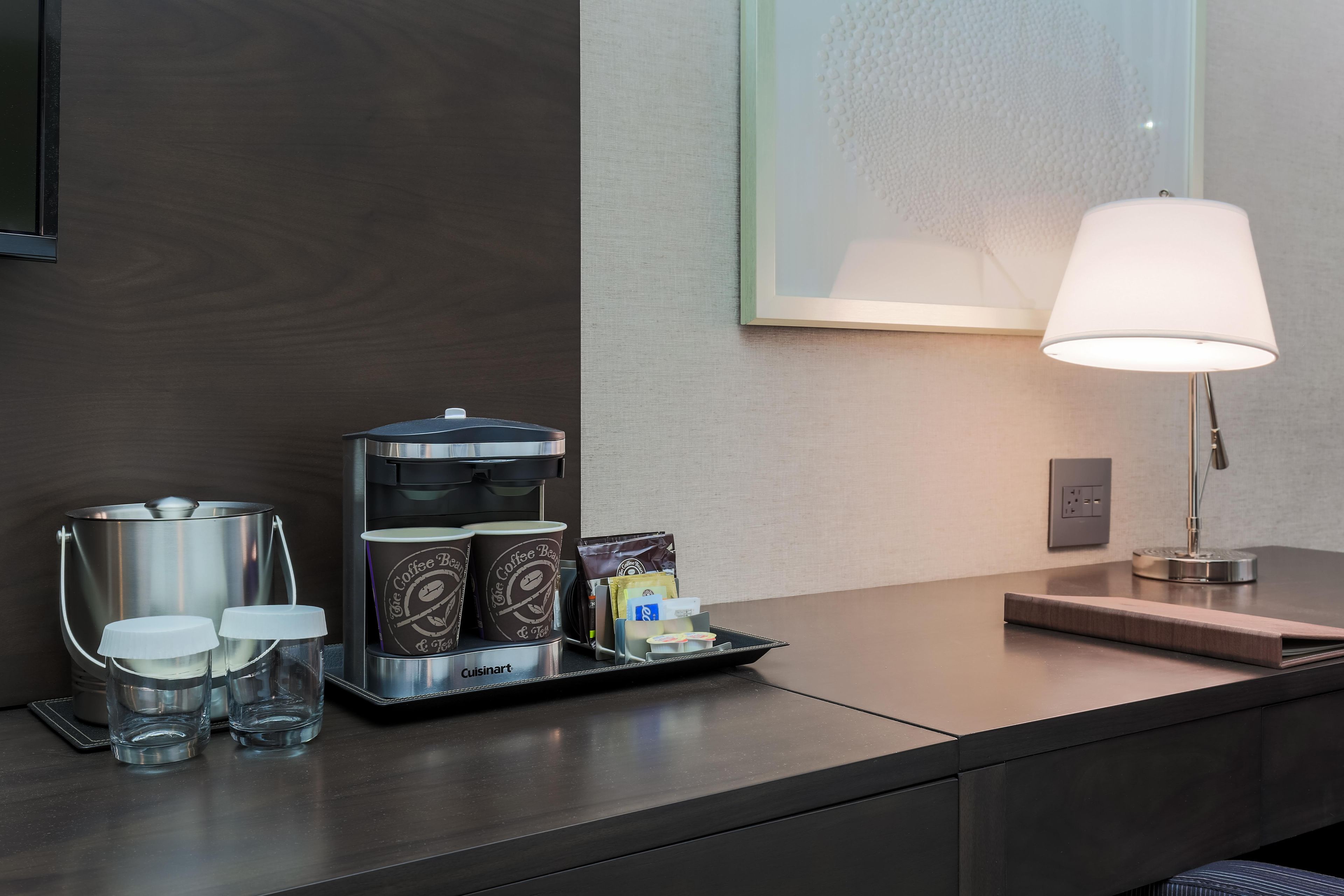 A hotel room's coffee station with a coffee maker, cups, and a tray of coffee pods.