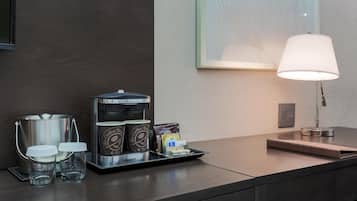 A hotel room's coffee station with a coffee maker, cups, and a tray of coffee pods.