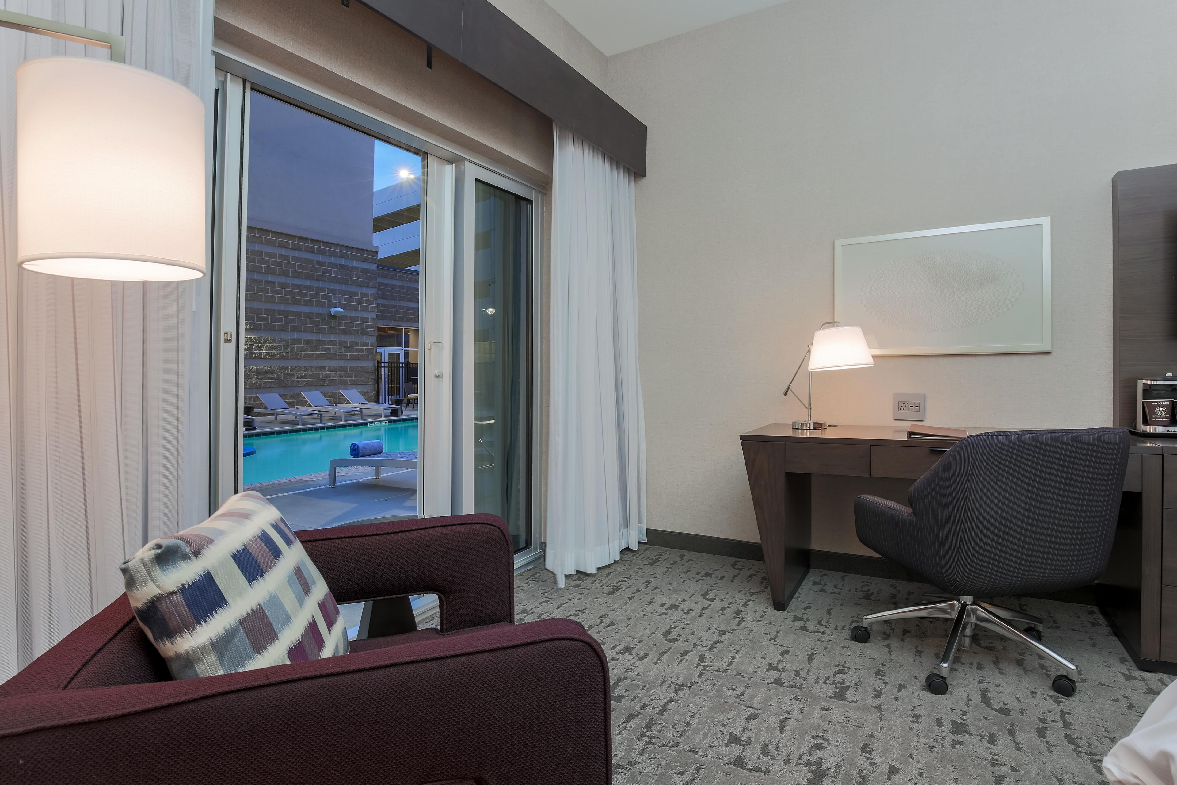 A hotel room with a desk, chair, and a view of a swimming pool.