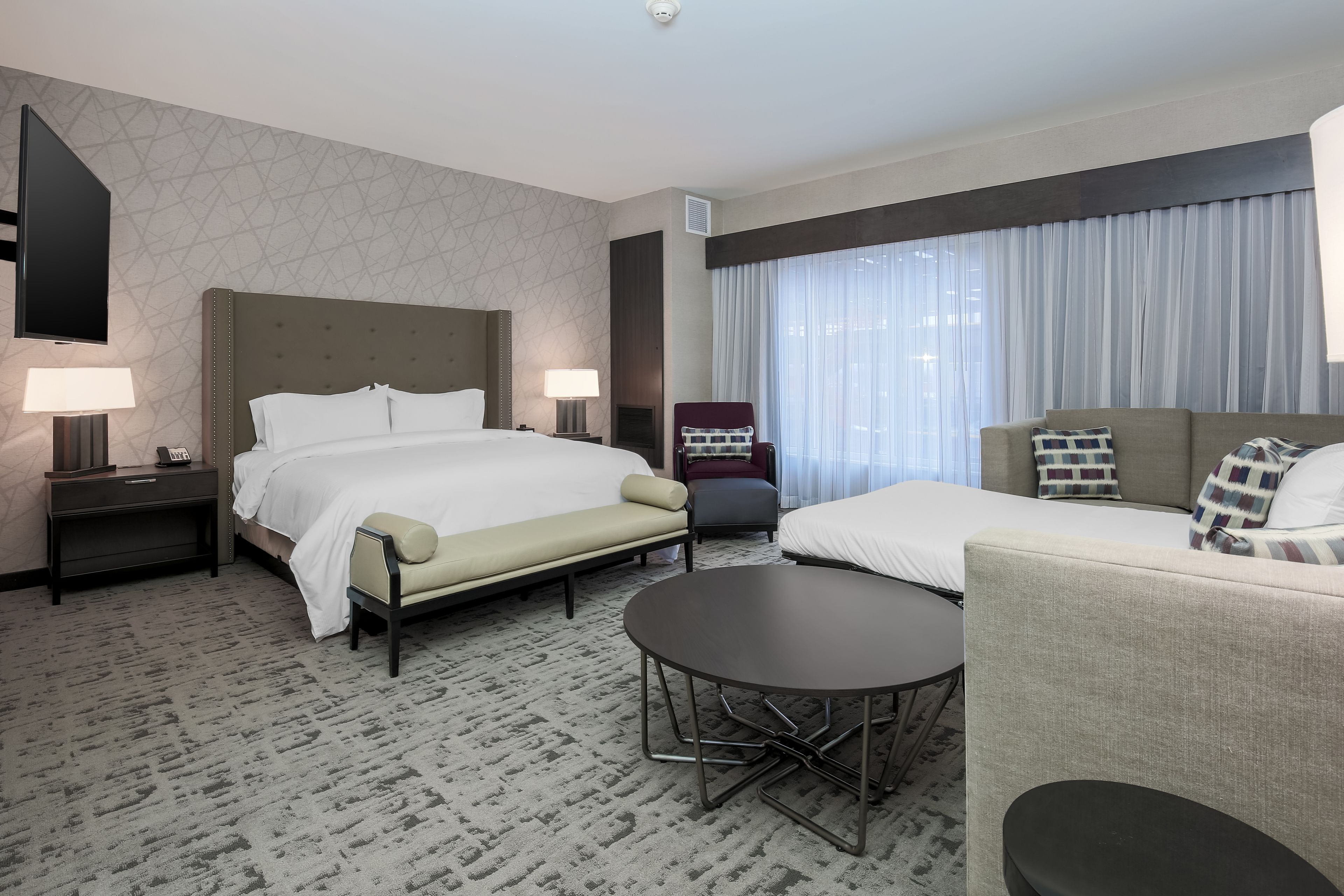 A hotel room with a large bed, a sofa, a small table, and a TV.