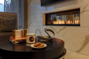 Ein modernes Wohnzimmer mit Kamin, Couchtisch mit Büchern, Keksdose und Teller mit Keksen.