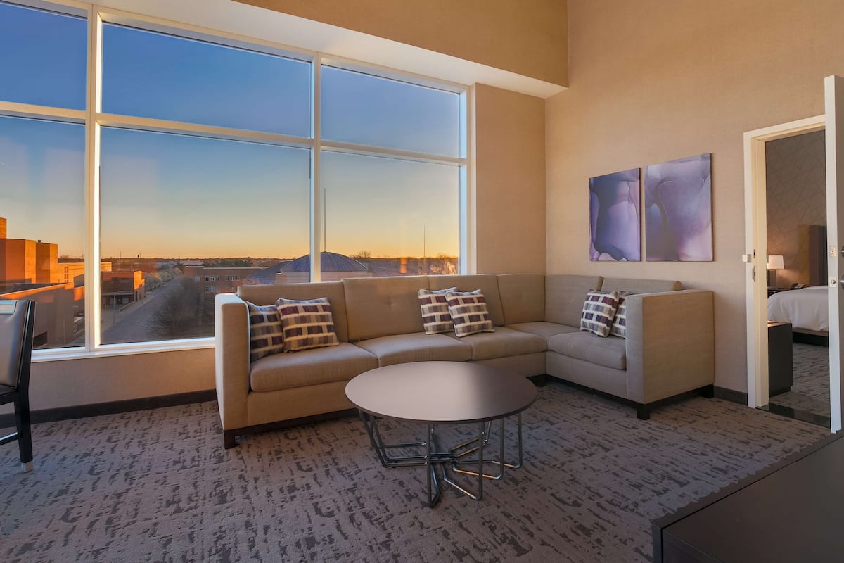 A modern living room with a large window, a sofa, a round coffee table, and two abstract paintings on the wall.