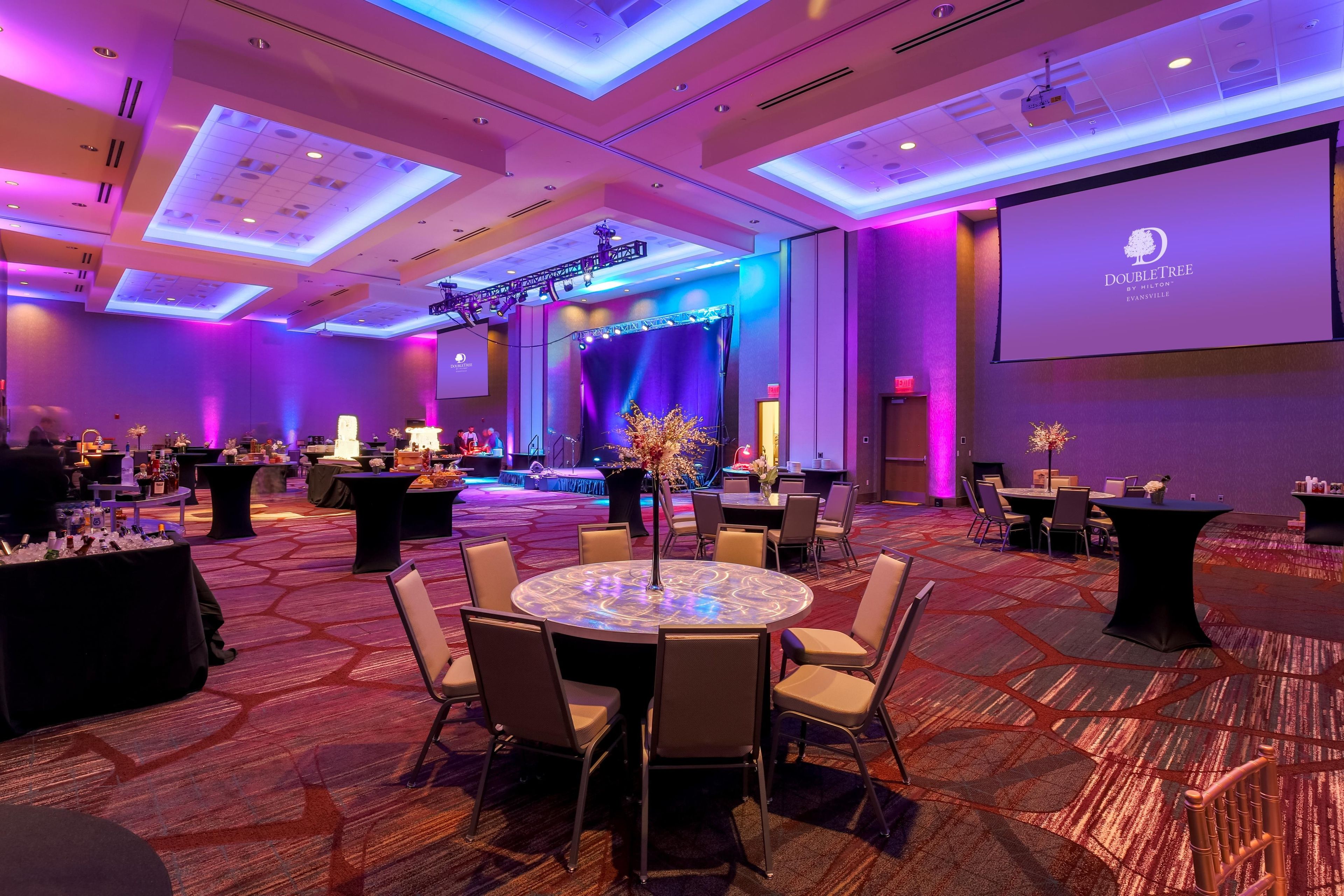 A conference room with a stage, tables, chairs, and a projector screen.