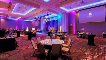 A conference room with a stage, tables, chairs, and a projector screen.
