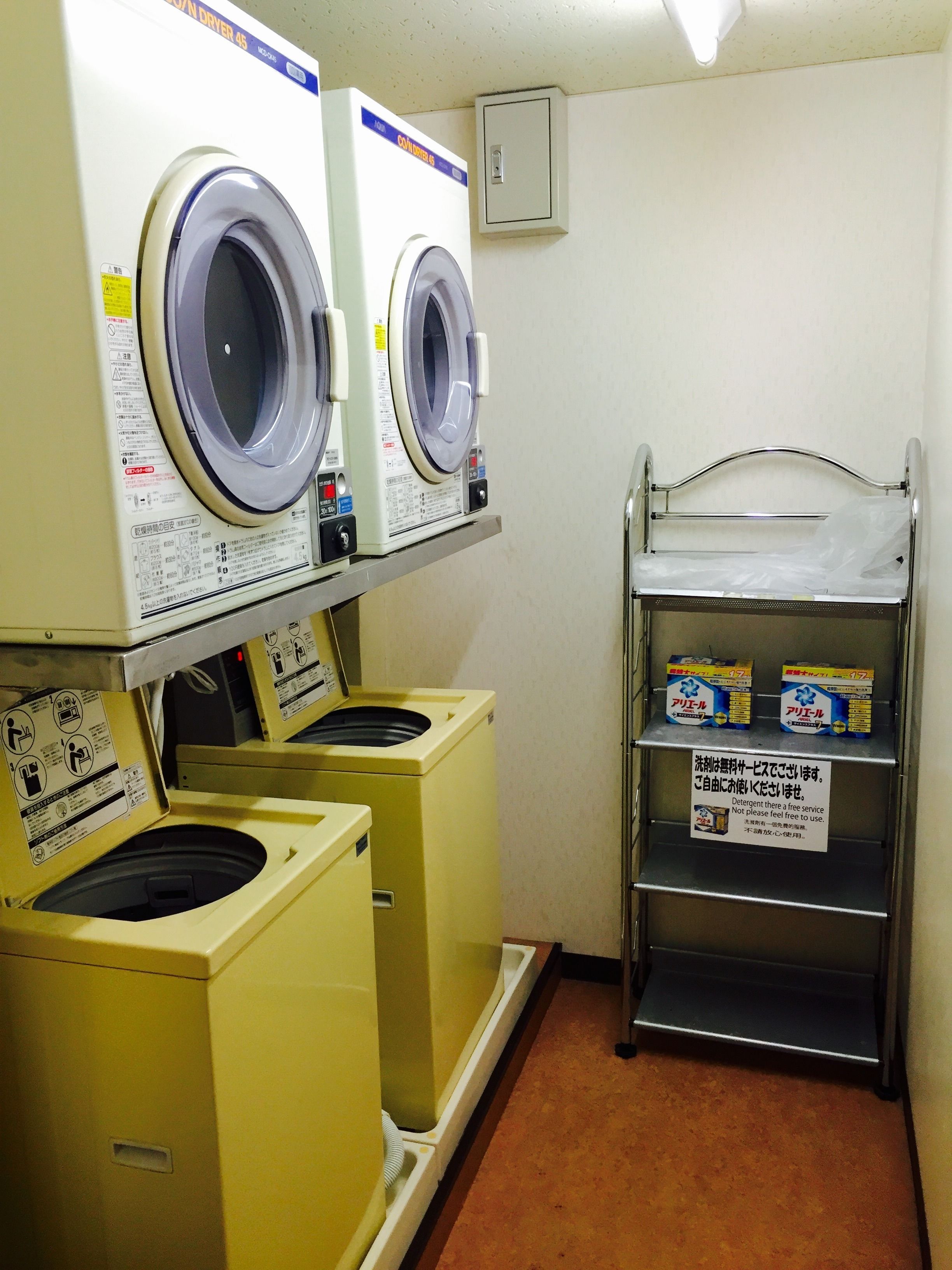 A laundry area with two front-loading washing machines, a drying rack, and detergent boxes.