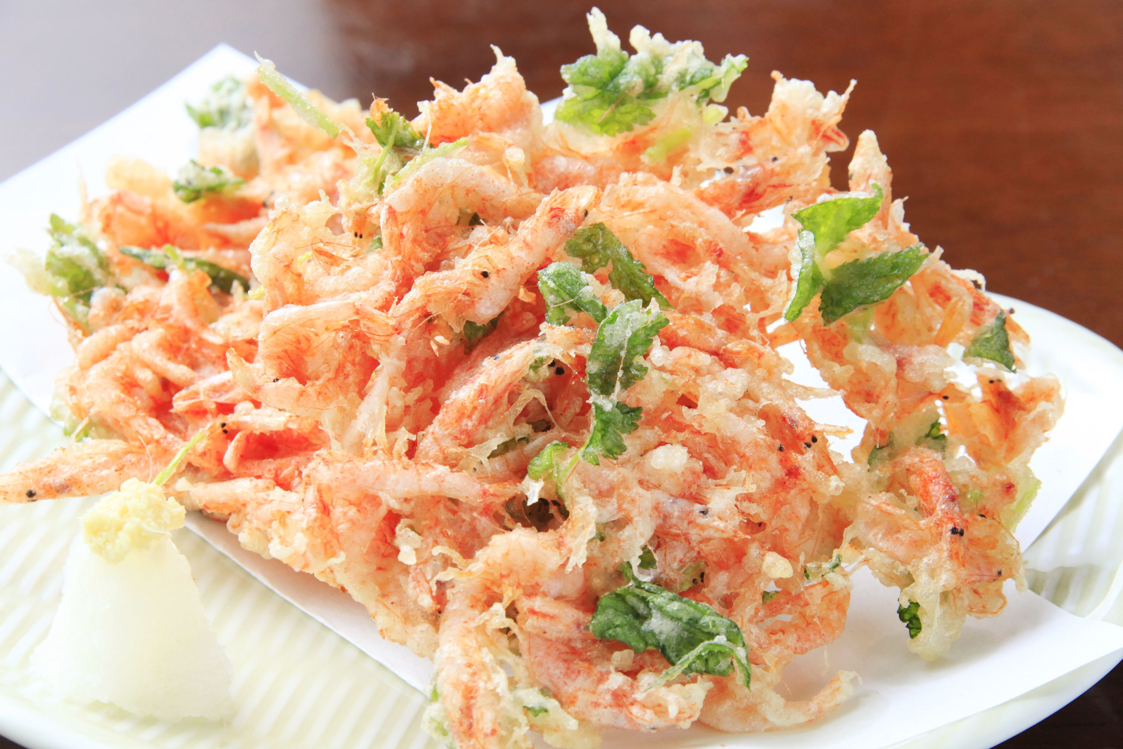 A plate of tempura shrimp with green herbs.