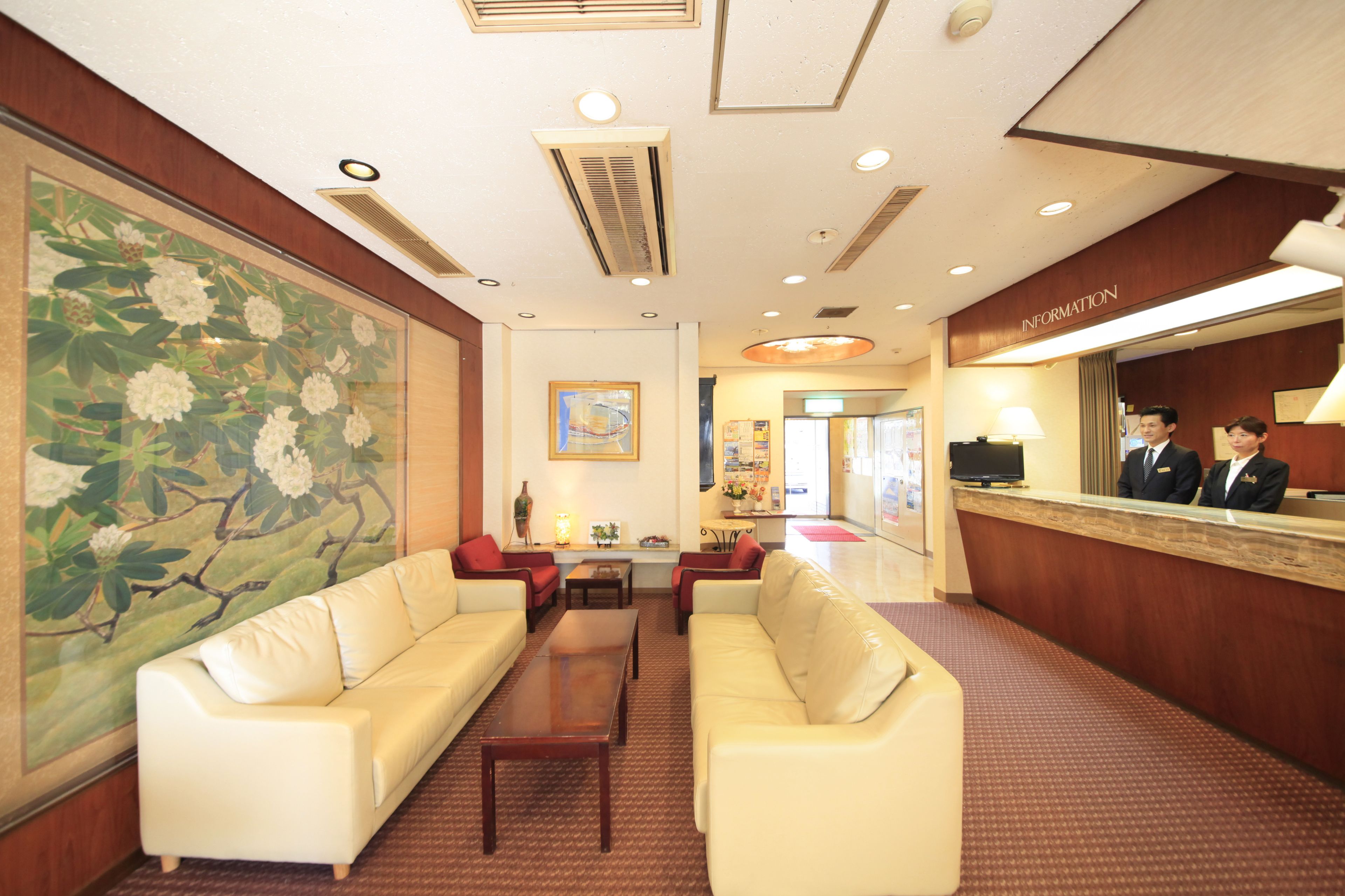 A hotel lobby with a reception desk, two sofas, a coffee table, and a large floral painting on the wall.