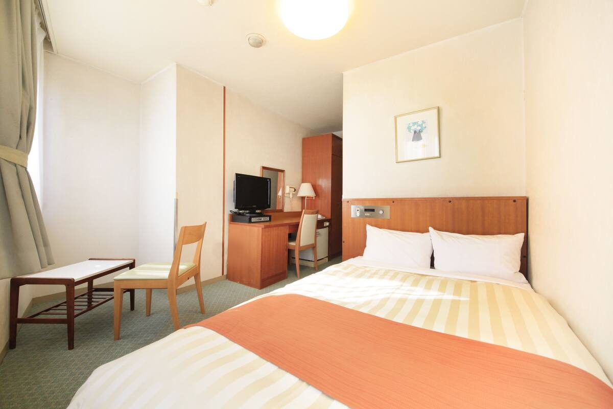 A hotel room with a bed, a desk, a chair, a television, and a picture on the wall.