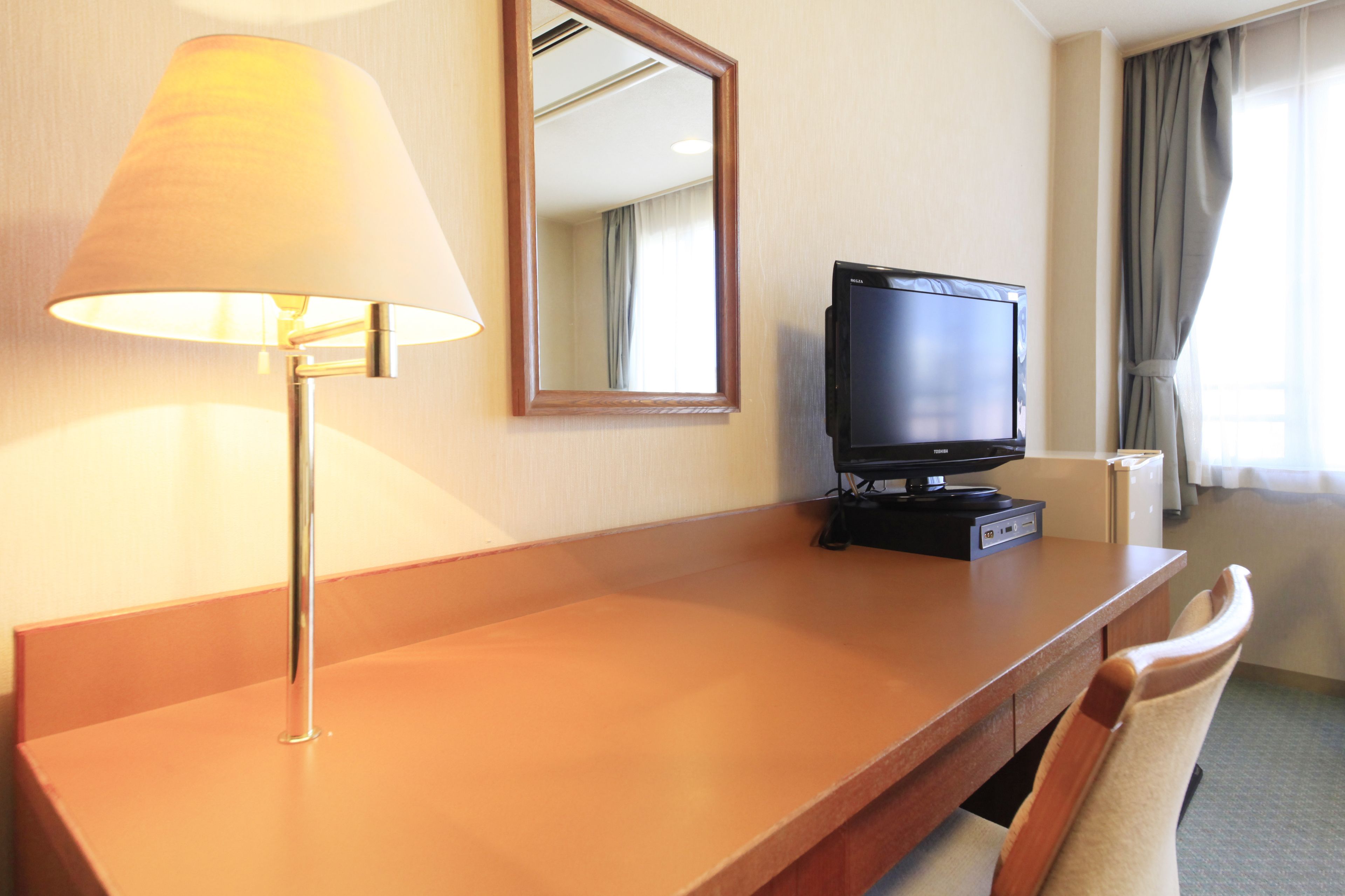 Habitación de hotel con un escritorio de madera, un televisor, una lámpara y un espejo.