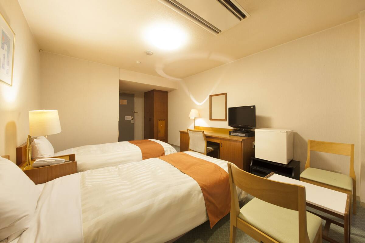 A hotel room with two beds, a desk with a television, a chair, and a lamp.