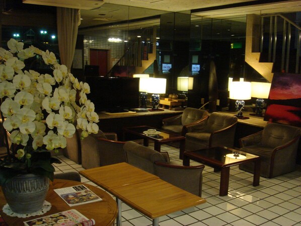 Et hotellobby med reception, siddeområde og et stort vindue med udsigt.