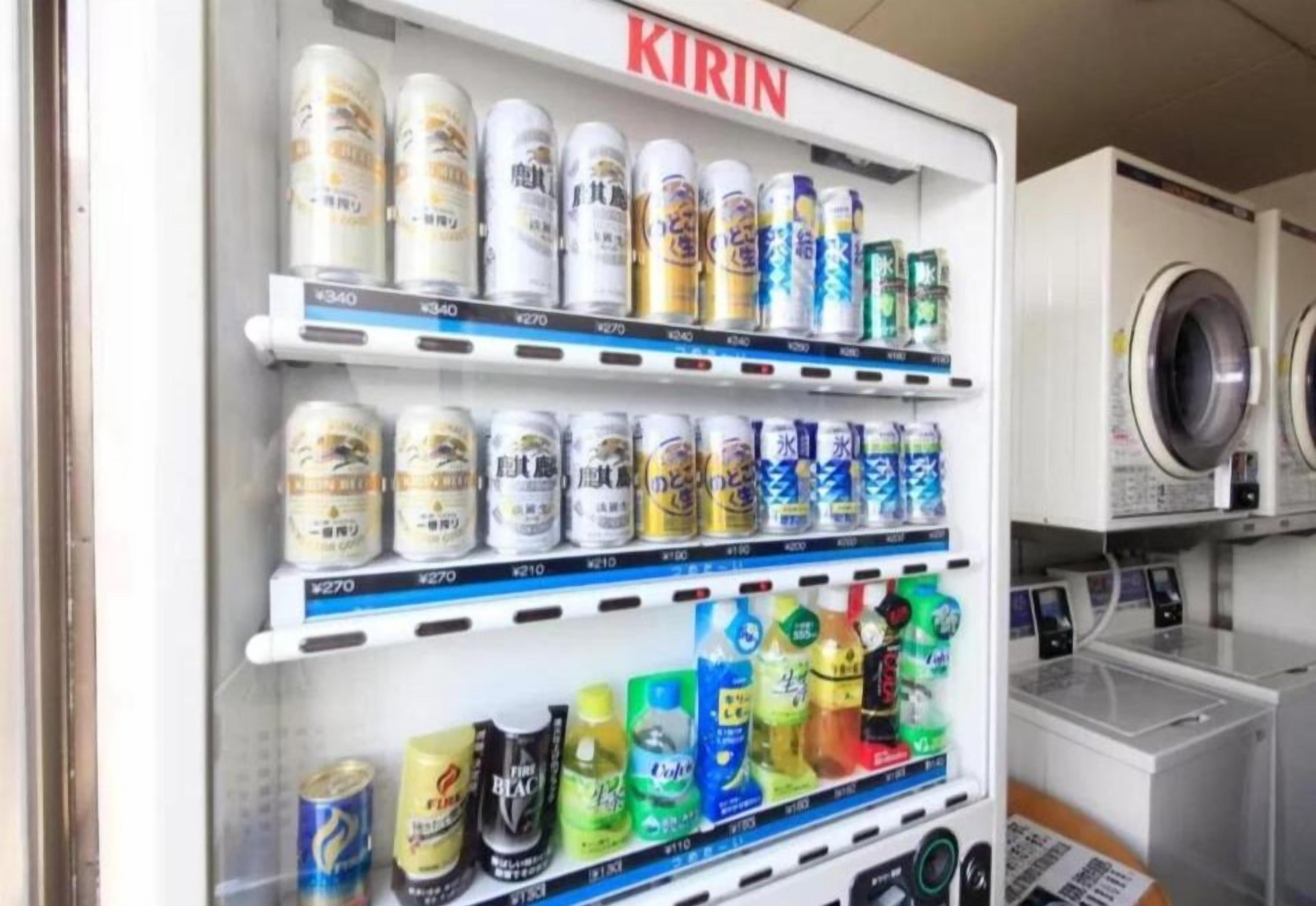 Un distributeur automatique proposant une variété de boissons et d’en-cas, notamment des canettes et des bouteilles, situé dans un lieu commercial.