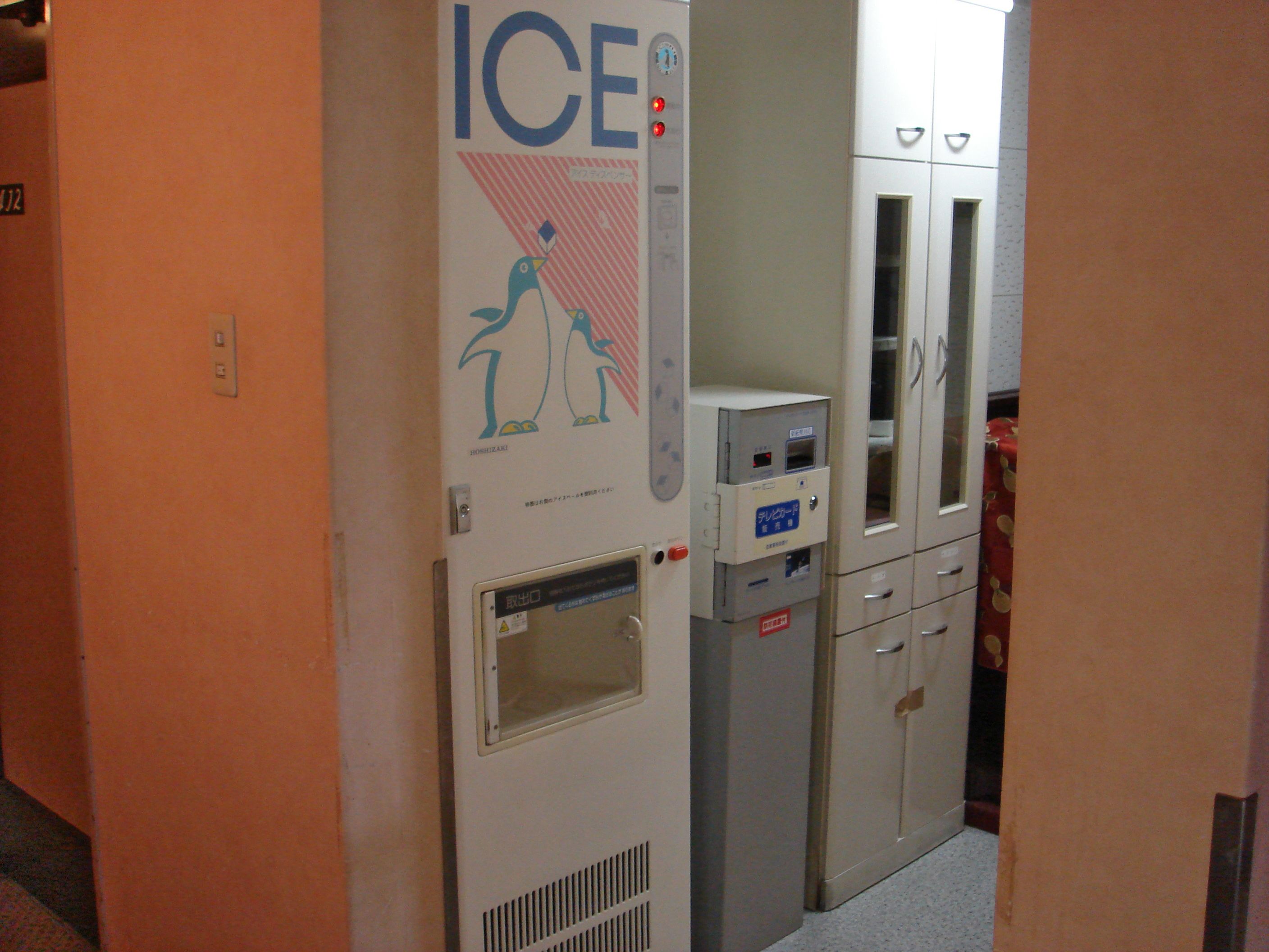 A hallway with an ice machine and a vending machine, cabinets, and a door with a number sign.