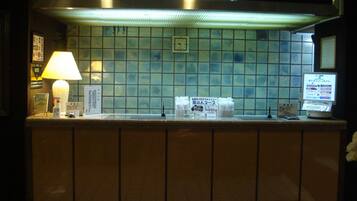 A reception desk with a lamp, a computer, and informational signs in a hotel lobby.