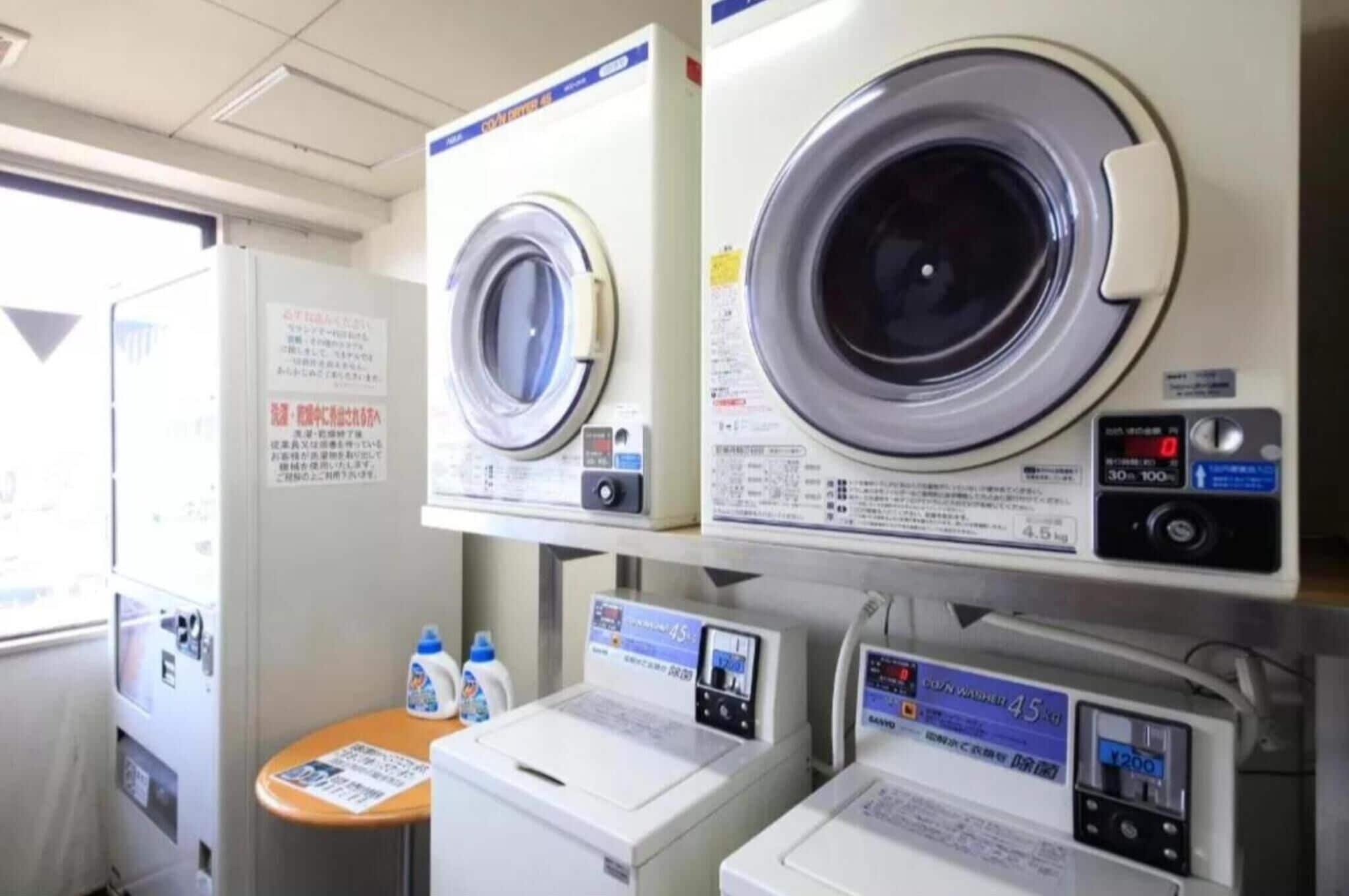 A laundry area with two front-loading washing machines, a small table with cleaning supplies, and a sign with instructions.