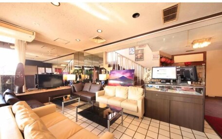 A modern hotel room with a living area featuring a sofa, a coffee table, and a TV. There is a small kitchenette with a refrigerator and a microwave.