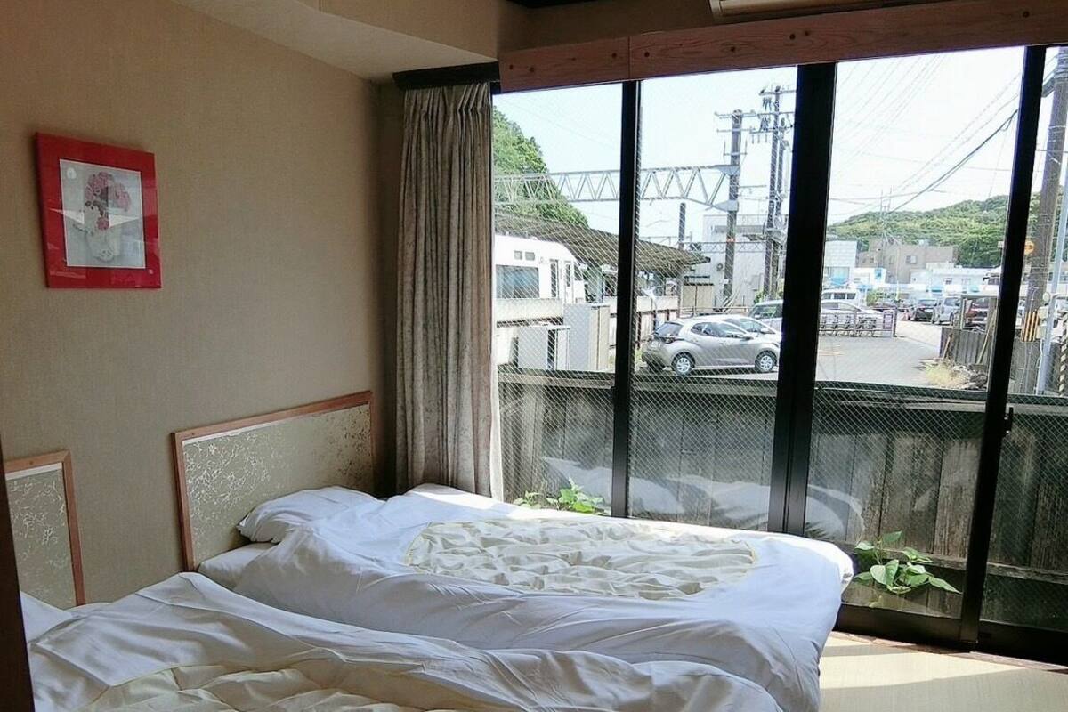 Een hotelkamer met twee bedden, een groot raam met uitzicht op de straat en een plafondventilator.