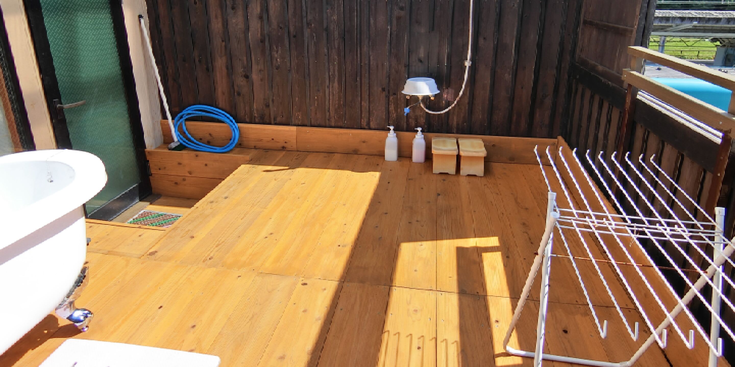 Une terrasse en bois avec une baignoire blanche, un tuyau d’arrosage et un étendoir.