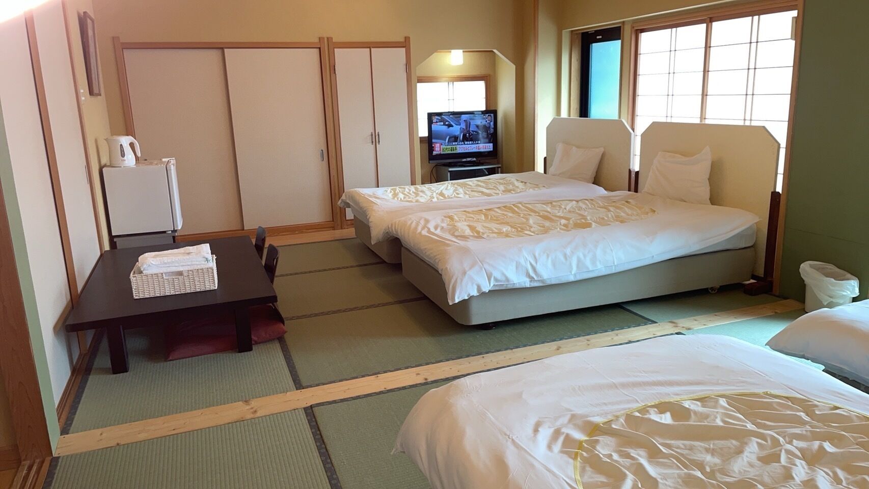 A hotel room with two beds, a small table, a TV, and a wardrobe.