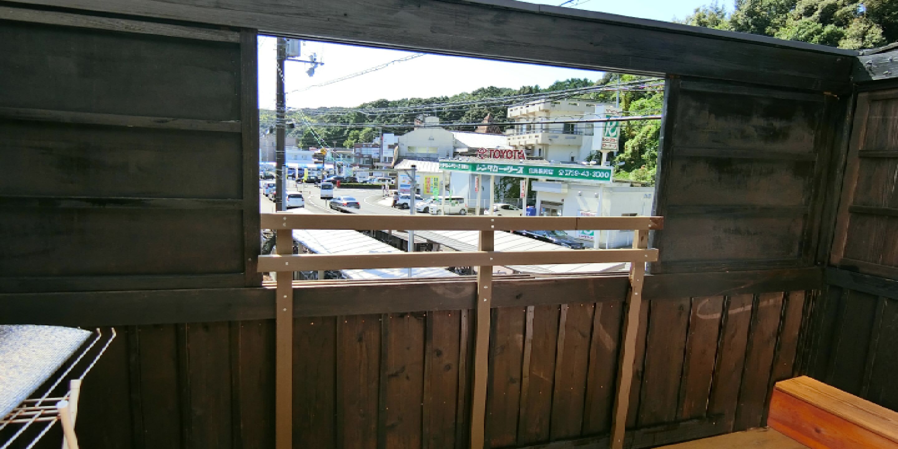 A view through a window with a wooden frame, looking out onto a street with buildings and parked cars.