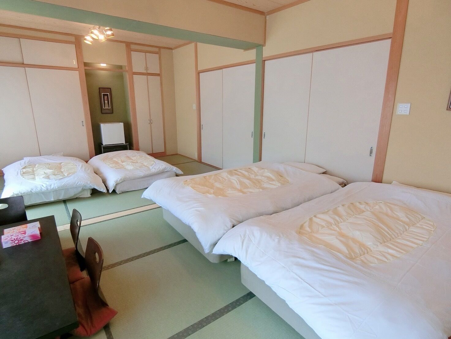 A traditional Japanese-style room with tatami flooring, three single beds, a small table with a chair, and a cabinet.