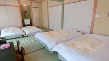 A traditional Japanese-style room with tatami flooring, three single beds, a small table with a chair, and a cabinet.