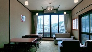 A room with a dining table, chairs, a sofa, and a large window with a view of the city. - Minshuku Inn Shirahama Ekinoyado (Shirahama)
