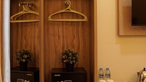 A wooden storage unit with multiple shelves, some containing potted plants, a safe, and a pair of slippers. - Hotel Cikini (Jakarta)