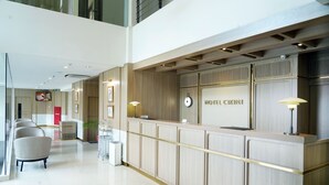 A hotel reception area with a modern design, featuring a reception desk, seating area, and a clock. - Hotel Cikini (Jakarta)