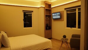 A hotel room with a bed, a TV mounted on the wall, a small table, and a chair. - Hotel Cikini (Jakarta)