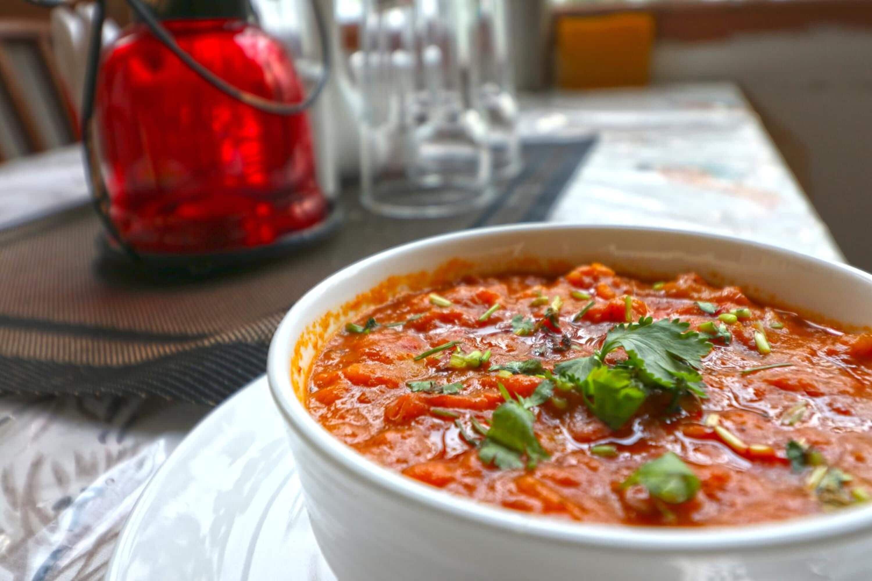 A bowl of soup garnished with herbs, placed on a table with a red candle and salt and pepper shakers in the background.