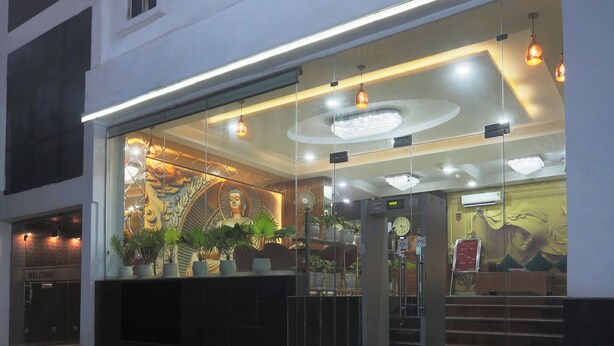 Entrada de hotel com fachada de vidro, uma estátua de Buda e um relógio.