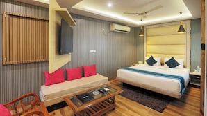 Quarto de hotel moderno com sofá, cama, mesinha de centro de vidro e ventilador de teto.