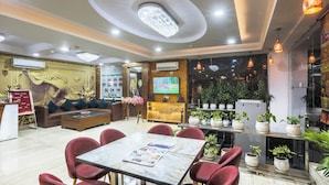 Um saguão de hotel com uma mesa de recepção, uma televisão, área de estar com cadeiras vermelhas e uma mesa de centro.