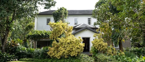 A white house with a dark roof, surrounded by lush greenery and a well-maintained lawn.