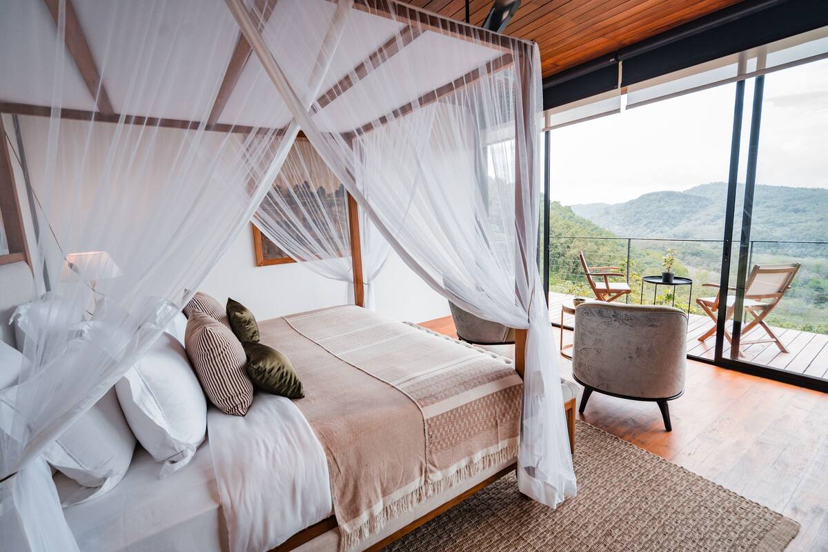 A bedroom with a large bed, a canopy, and a view of the outdoors.