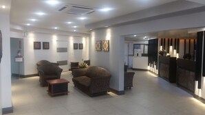 A modern reception area with a reception desk, seating area with sofas and armchairs, and a wall-mounted information board. - Peninsula International Hotel (Suva)