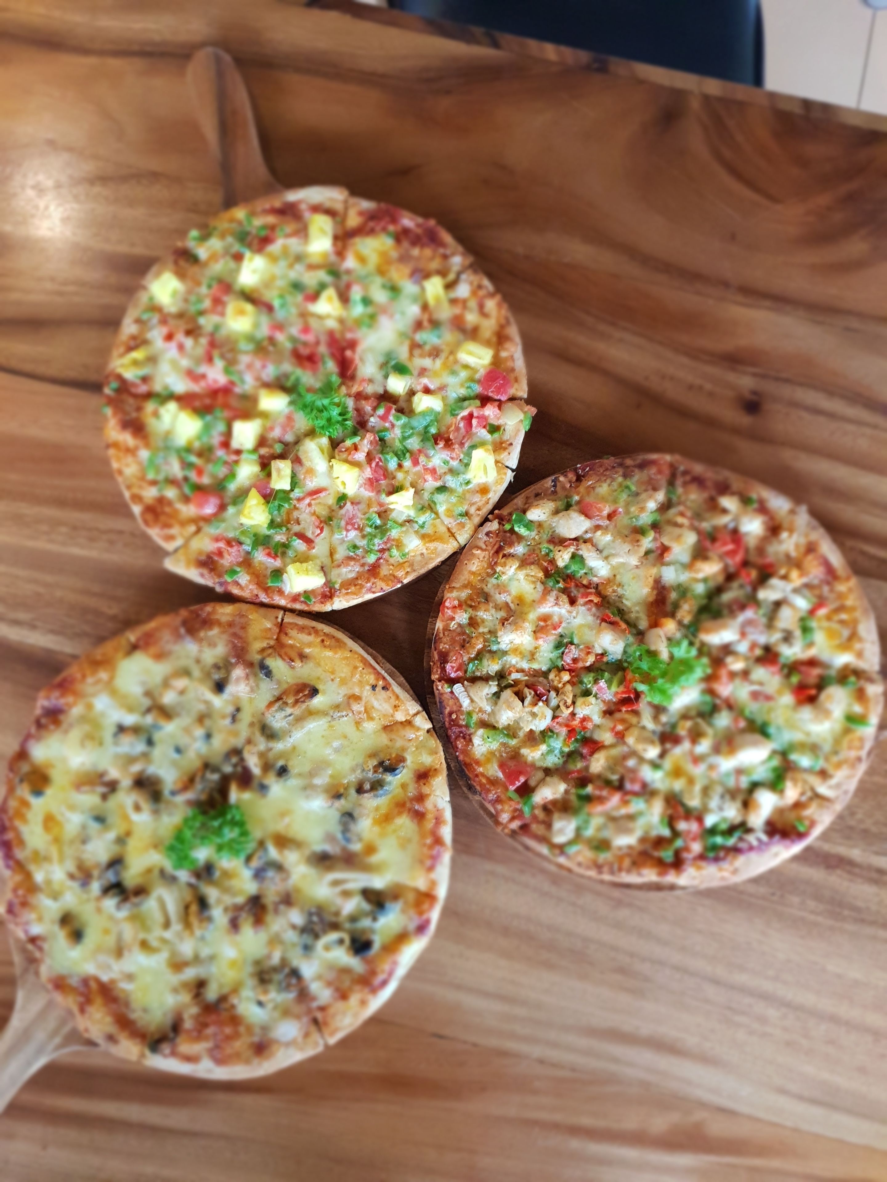 Three pizzas on a wooden table.