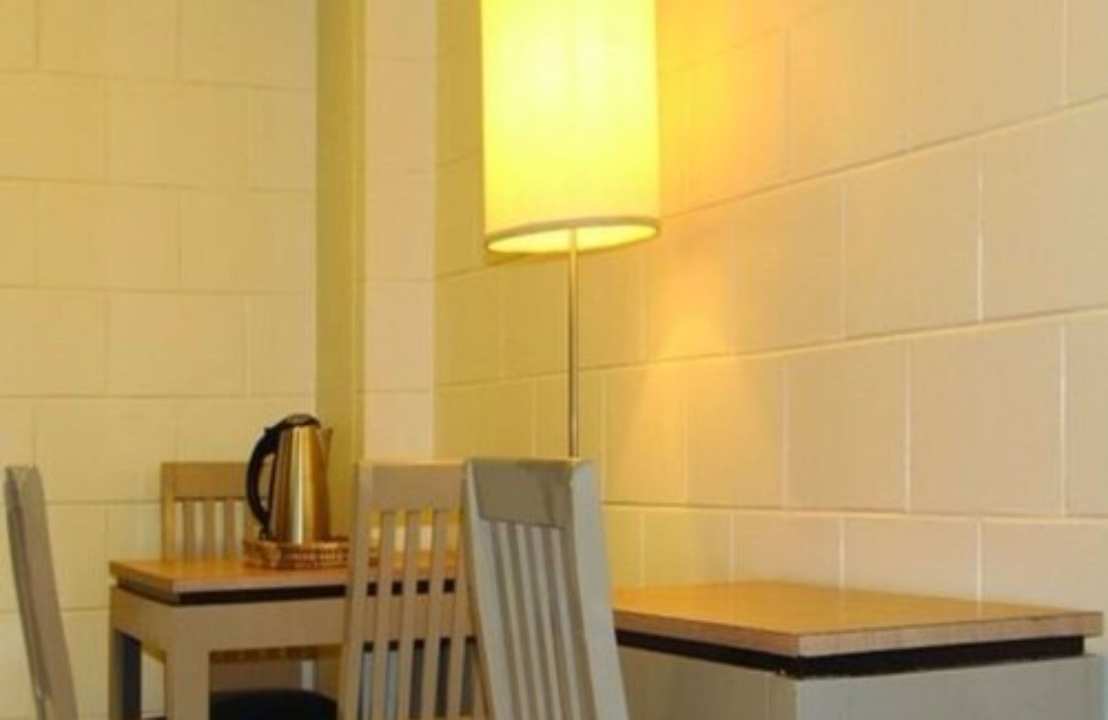 Un pequeño comedor con una mesa y dos sillas, una lámpara y una cafetera sobre la mesa.