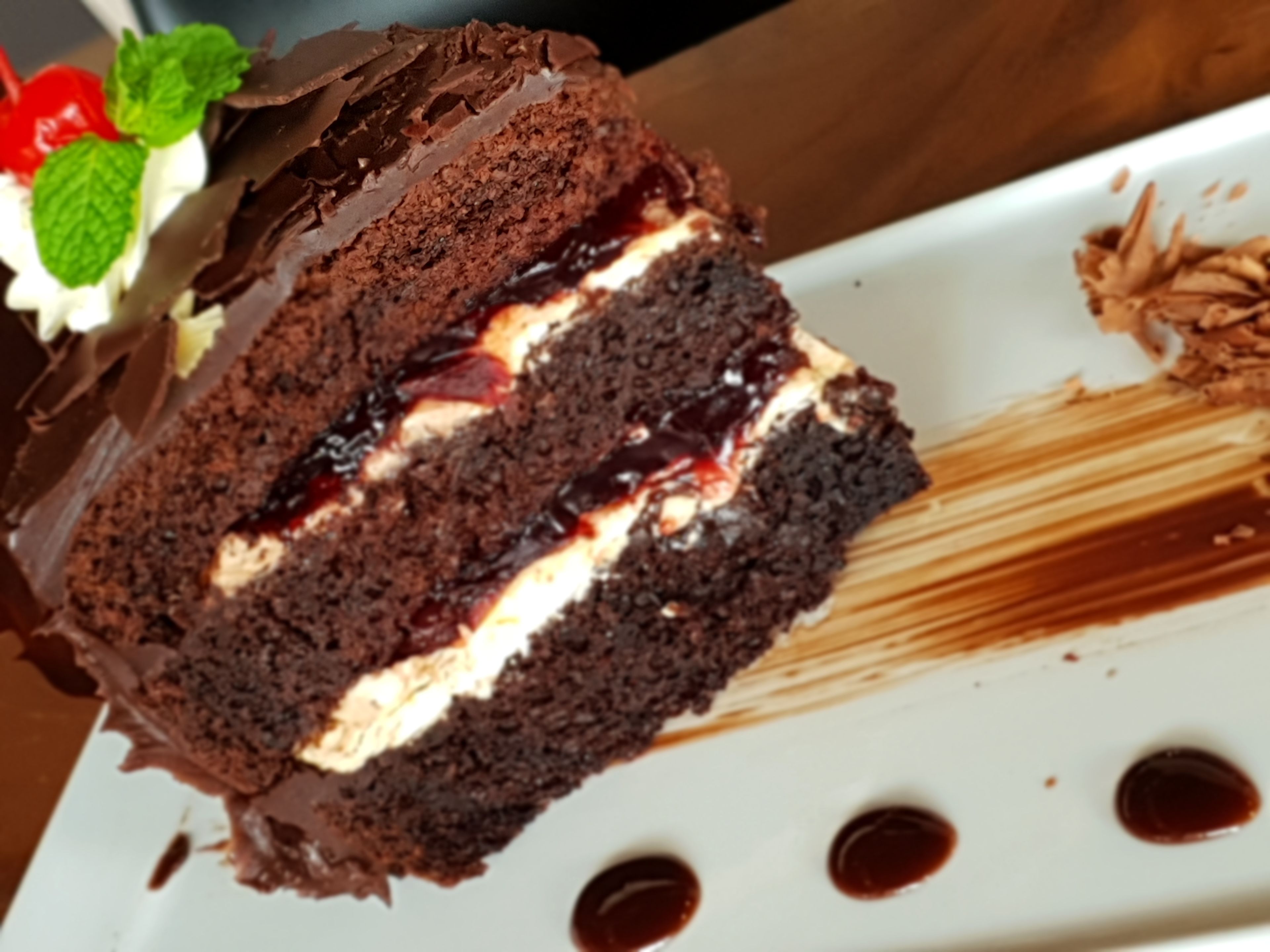 Ein Stück Schokoladenkuchen mit Sahne und Früchten auf einem weißen Teller.