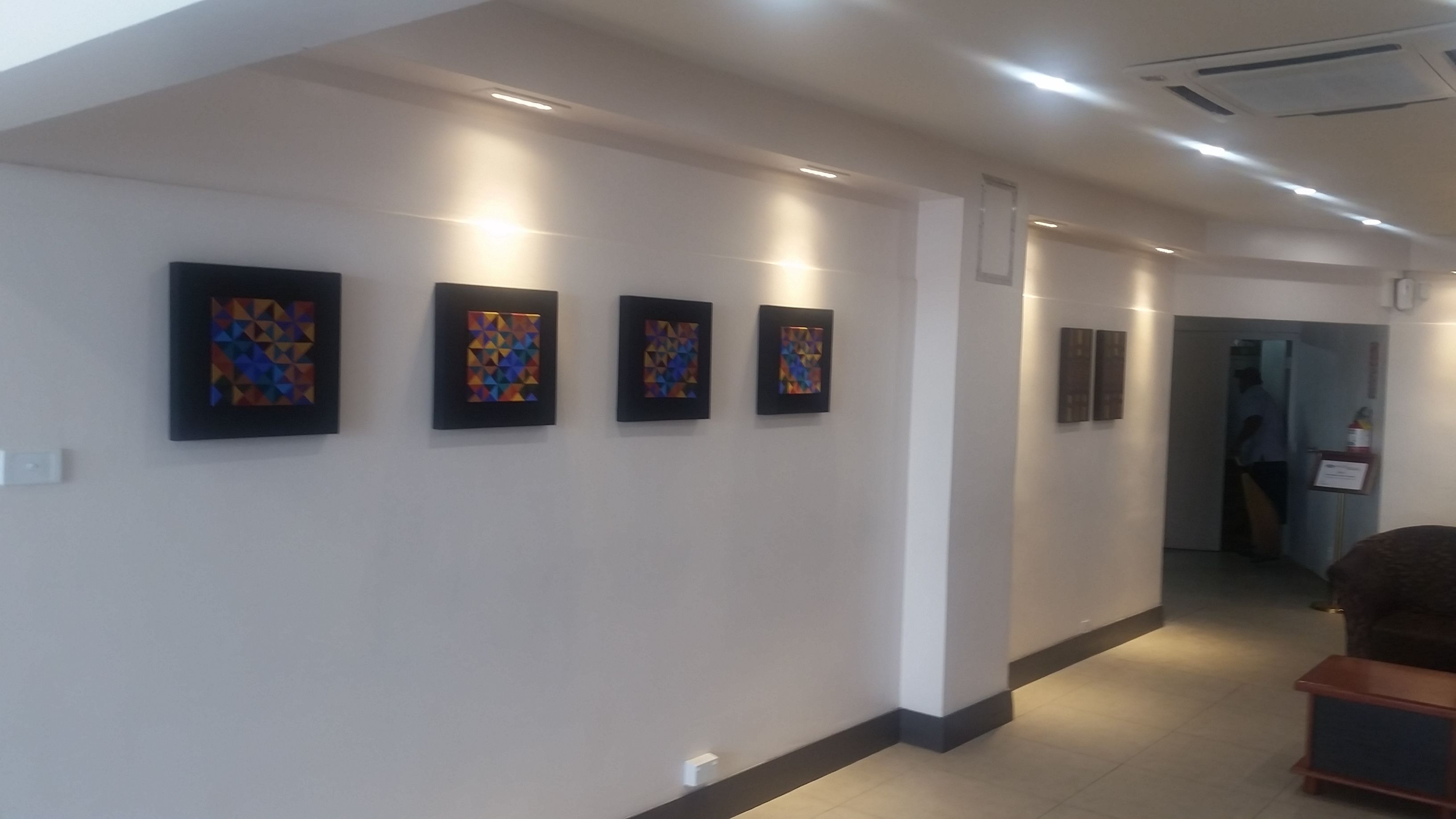 A hallway with four framed artworks on the wall, a door at the end, and a small wooden bench in the foreground.