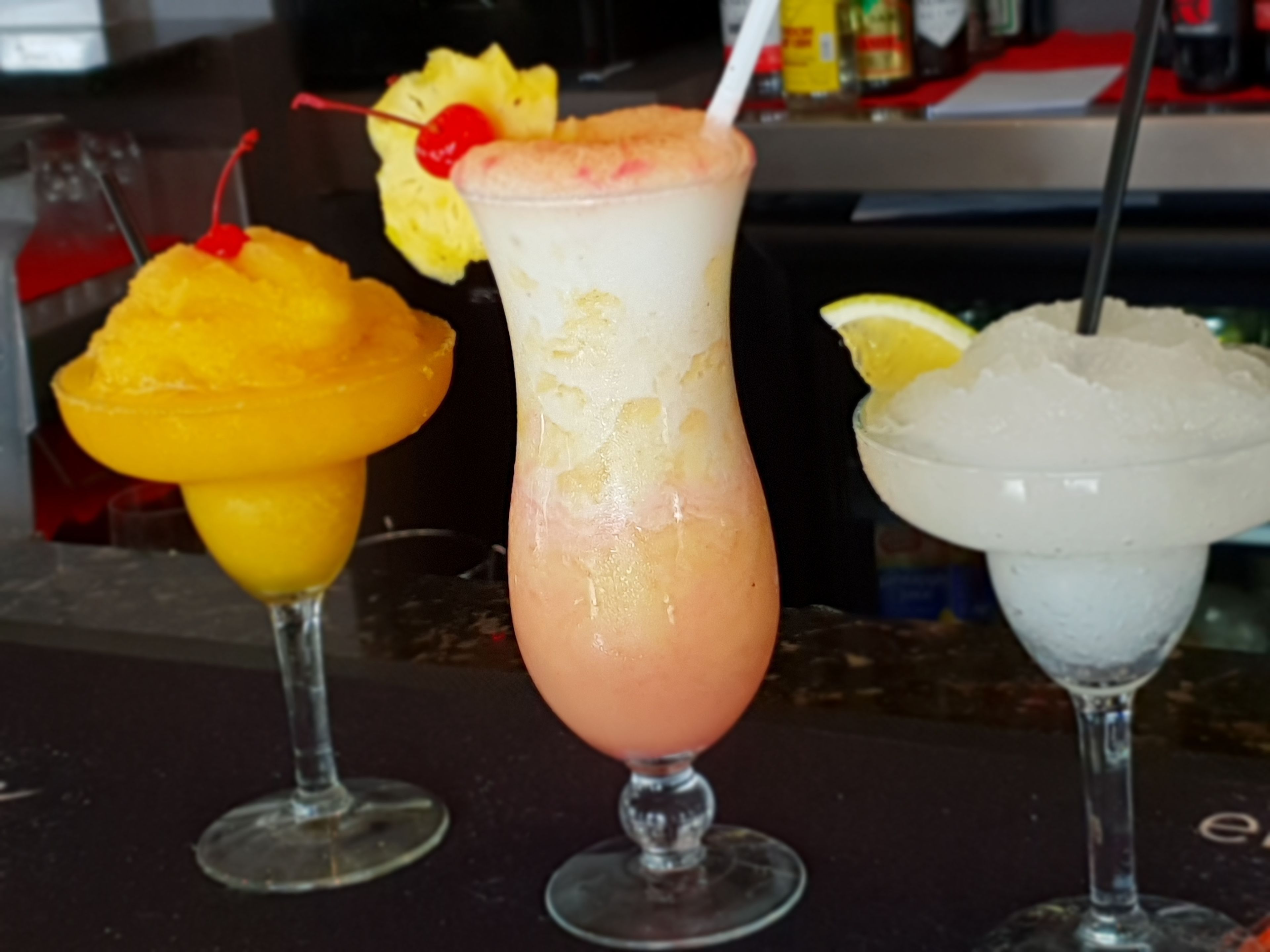 Three drinks on a bar counter, each with a different garnish.