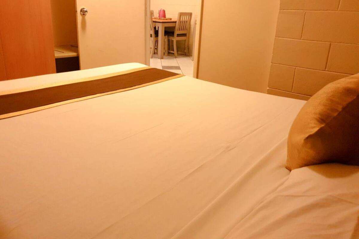 A hotel room with a bed, a wooden door, and a view of a dining area with a table and chairs.