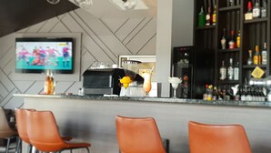 A modern bar area with a flat-screen TV, bar stools, a coffee machine, and a variety of bottles on shelves. - Peninsula International Hotel (Suva)